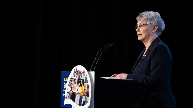 A white woman with short grey hair speaks at a podium.