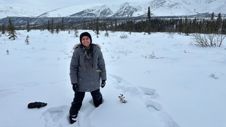 A woman stands in a barren snowy landscape with mountains in the background.