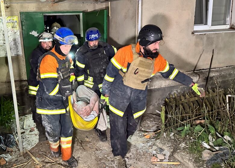 Rescuers carry a man, whose head is covered in dust, in a sleeve stretcher as they exit a building.