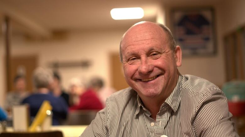 A man in a stripped collared shirt smiles at the camera with a group of women in the background.