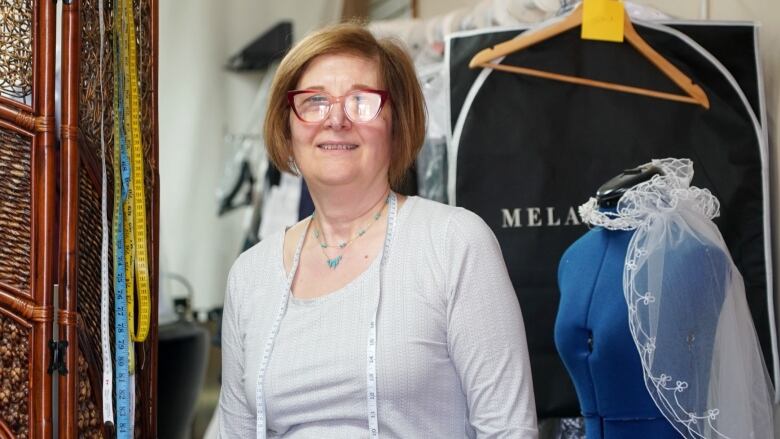 A woman with glasses stands in the middle of a tailor shop.