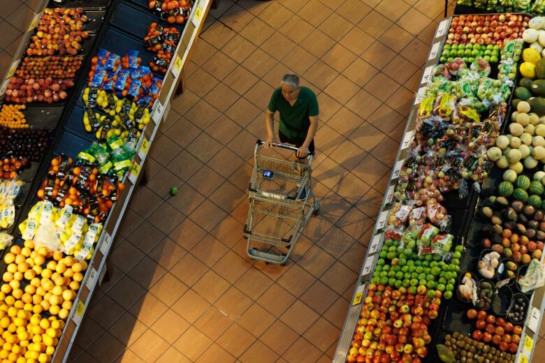 A man pushes a  grocery cart in the produce aisle of a grocery story