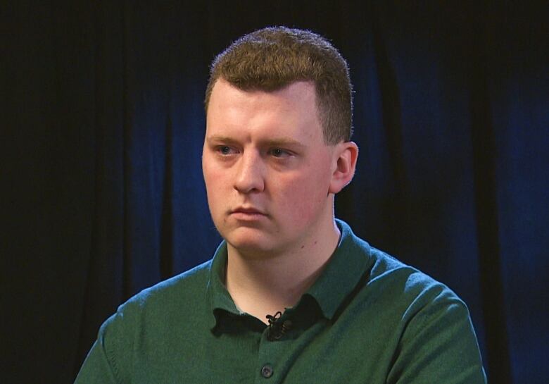 A head and shoulders shot of a young man wearing a green shirt. The background is dark.