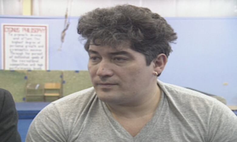 A man with dark hair sits in a gym.