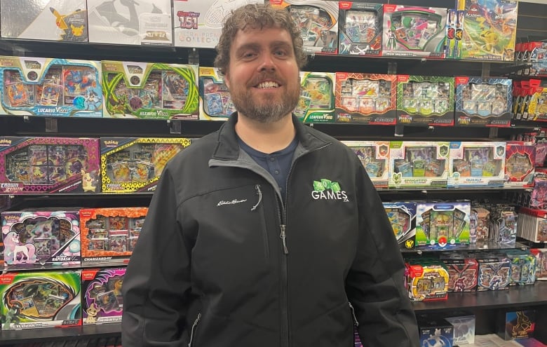 A man stands in front of store shelves stocked with Pokmon cards, packs and boxes.