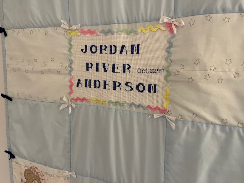 A blue and white baby blanket embroidered with the name 