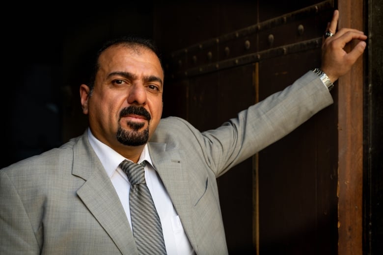 A portrait of Zaid Saadallah. He had dark brown hair and a goatee. He is wearing a grey suit a white shirt and a grey striped tie. 