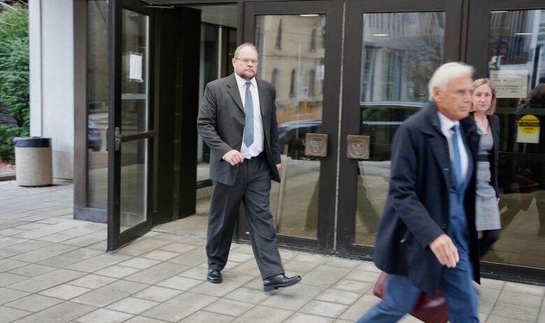 A man wearing a suit walks out of a building. 