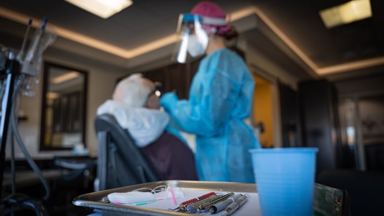 A dental hygienist cleans a senior's mouth, her tools are diplayed in the foreground.