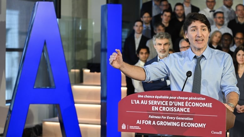 A man stands in front of a sign and a group of people.