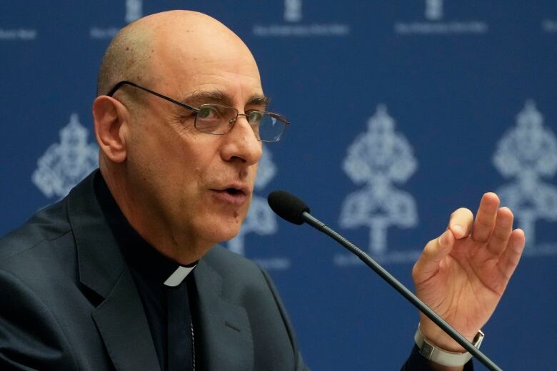 A man wearing catholic priest attire speaks into a microphone