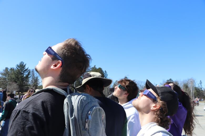 People wearing eclipse glasses look at the sun.