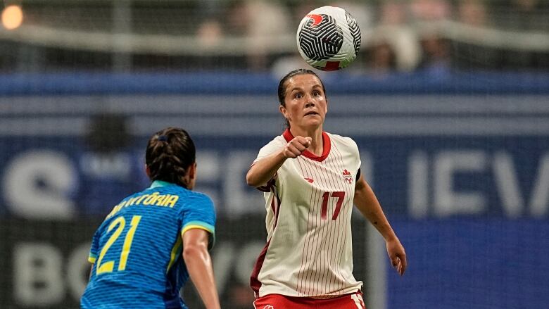 Women's soccer player keeps her eye on the ball above her head has an opposing player defends her.