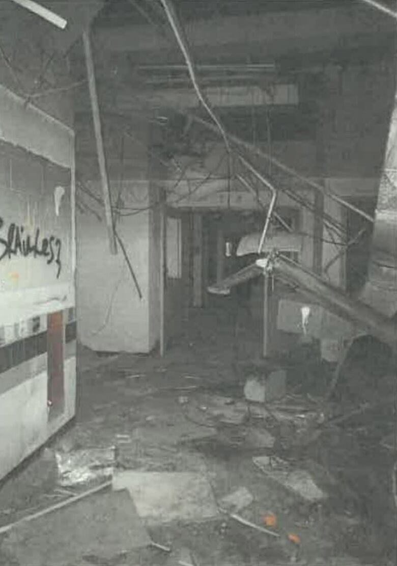 A black and white photo shows construction debris on the floor, graffiti on a wall and silver ducts hanging from a ceiling