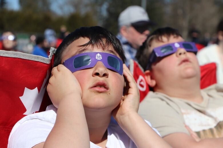 A kid wears eclipse glasses as he looks up at the sun.