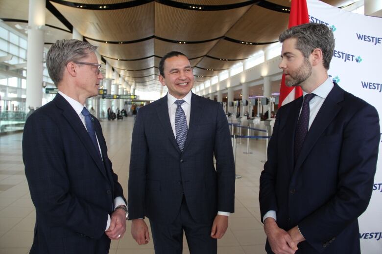 Three men wearing suits stand inside a building.