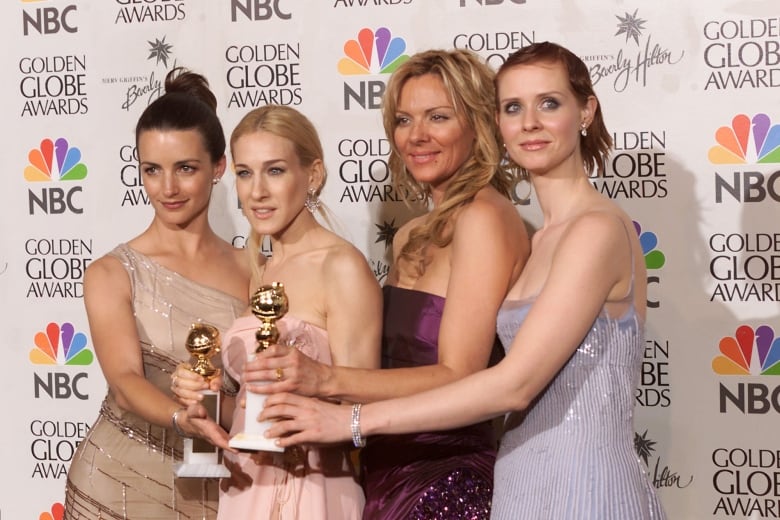 Four women in gowns  hold a  trophy