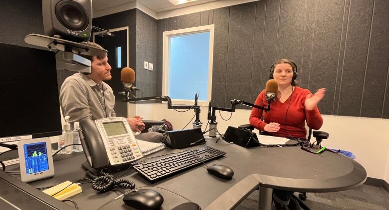 Man and woman speaking into microphones in radio booth.