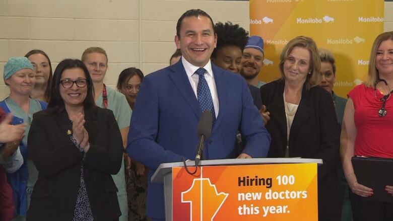 A man is pictured speaking at a podium, in front of a group of people.