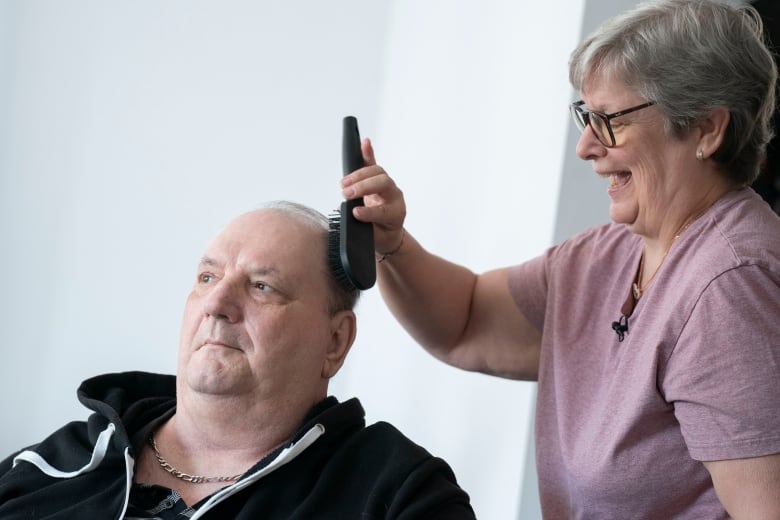 A woman smiles while brushing a man's heair 