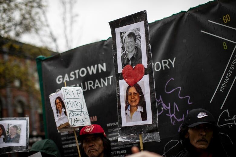 People holding signs depicting photos of victims who who were found dead in the aftermath of a fire that gutted a hotel in Vancouver.