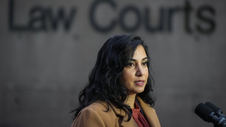 A South Asian woman with dark brown hair and a brown coat stands outside the courthouse.