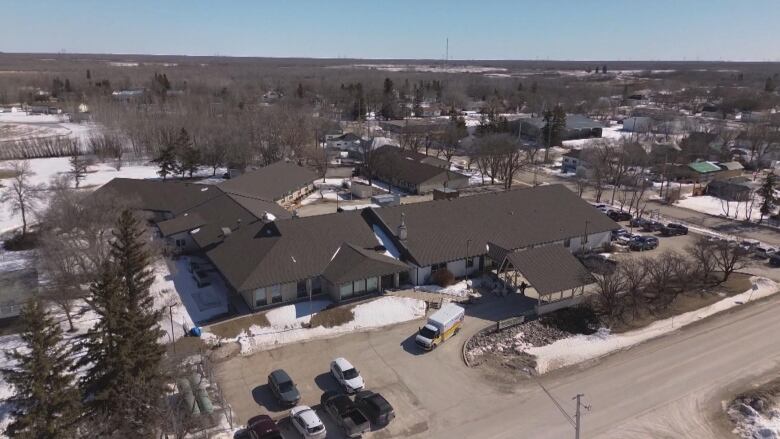 An aerial view of an ambulance leaving the bay outside a hospital with a brown roof.