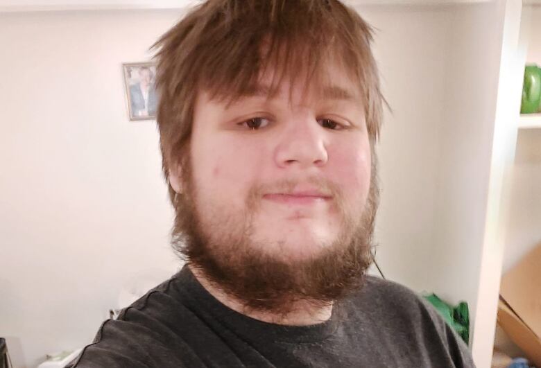 A young man with a beard and wearing a black T-shirt takes a selfie.