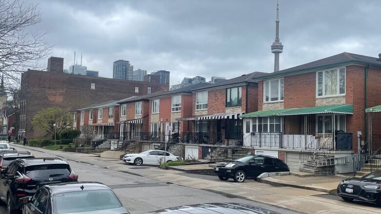 On a grey, rainy day, Row houses on an empty city street with the CN Tower rising above them