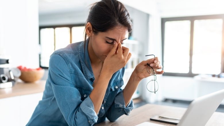 A woman sits at a laptop looking stressed