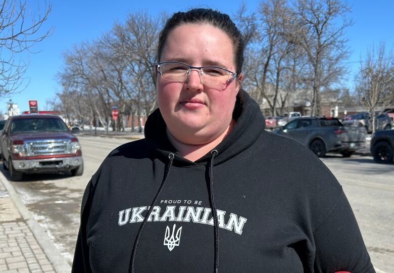 A woman wearing a black hoodie is pictured on a small town's main street.