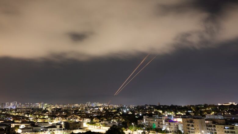 Streaks of light are seen in the night sky over a city.