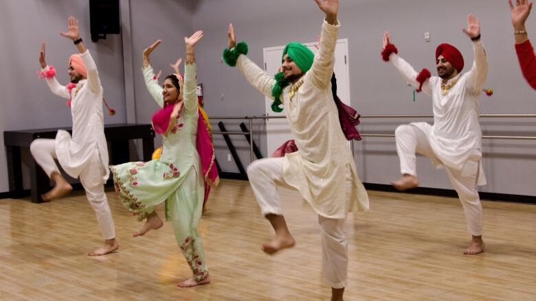 A group of two women and three turbaned men in colourful Indian outfits dance with smiles on their faces. 