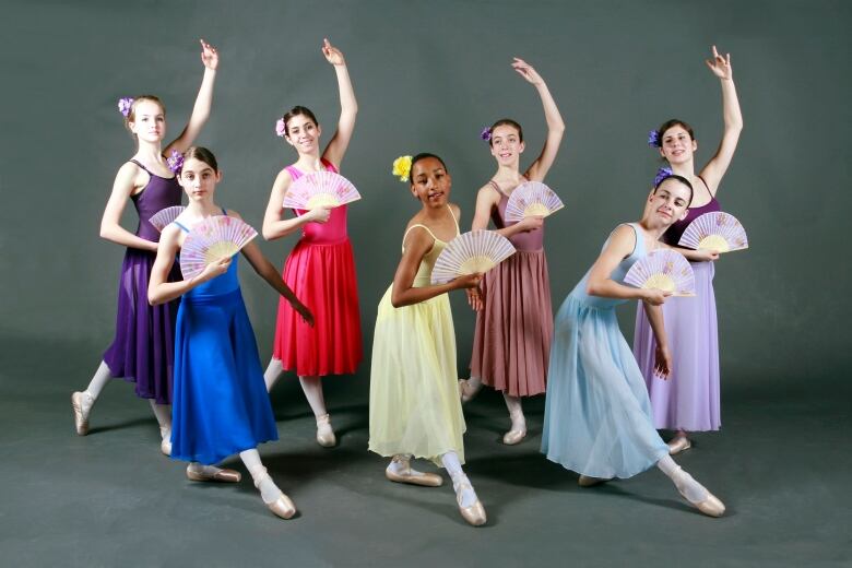 A group of young ballet dancers pose against a grey backdrop. A lone black dancer poses in the middle among her white peers. 