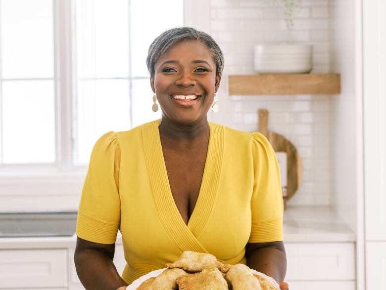 A portrait of a woman in a yellow dress holding a plate of pastries. 