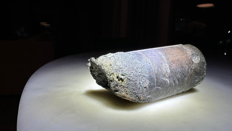 A piece of disfigured metal sits on a white counter, with a light shining on it.