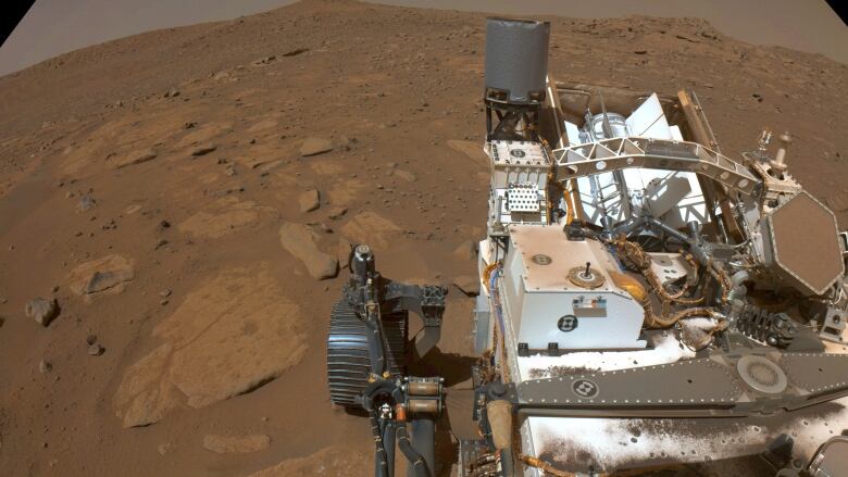 A robotic rover sits on a red, rocky surface.