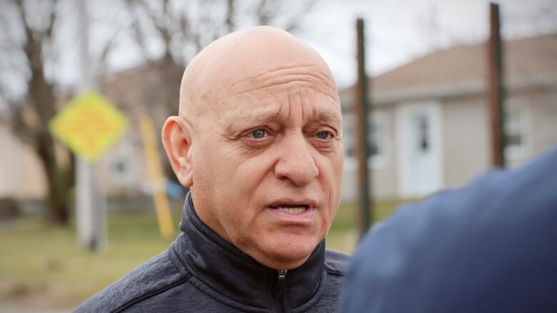 A bald man with a blue jacket speaks to another man.