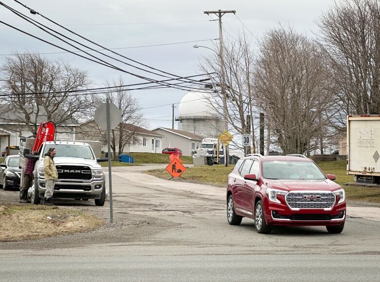 A red vehicle pulls out of an intersection leading to a residential neighbourhood with a large white radar dome looming in the background.