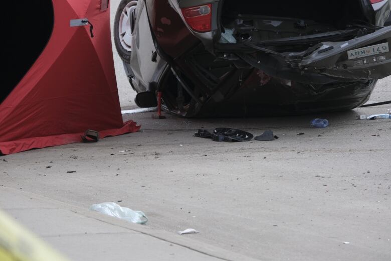 there is an upside down vehicle, car pieces scattered on the road, and police walking around