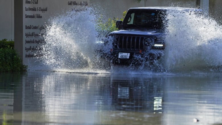 Water splashes up as a white SUV drives through flooding following heavy rainfall in Dubai.