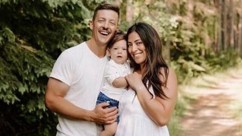 A man and woman are seen smiling and holding a baby between them.