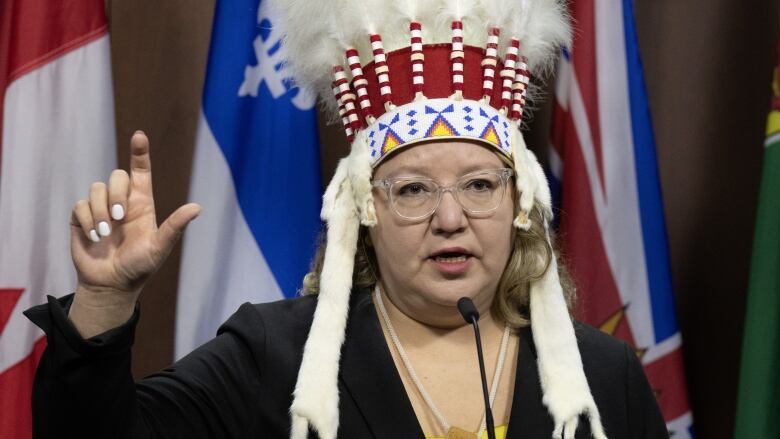 A woman in a headdress gestures while speaking at a podium.