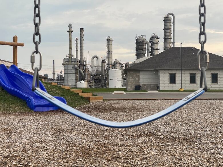 A playground swing is shown and in the background is an industrial plant.