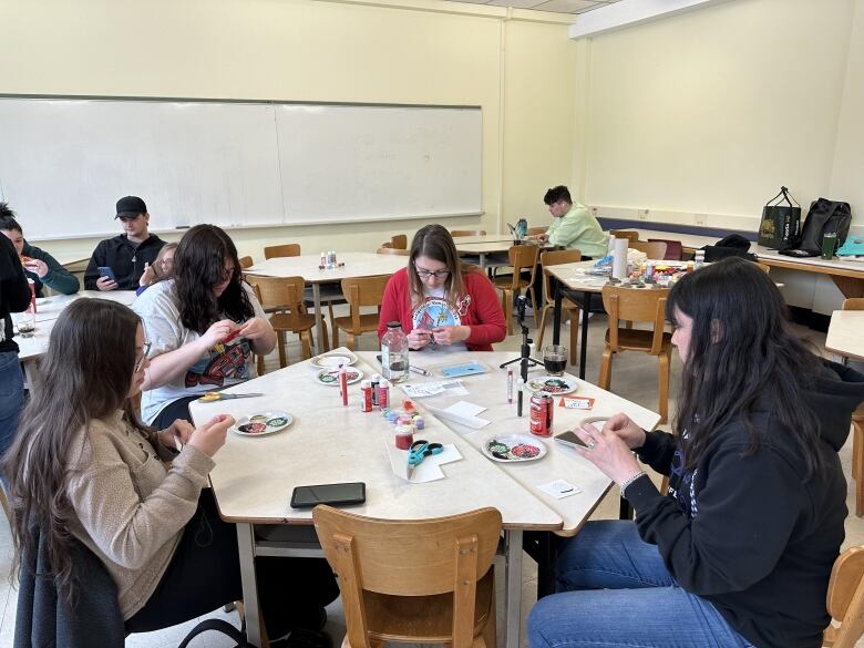 A group of people sit at a table in the shape of a hexagon doing various beading.