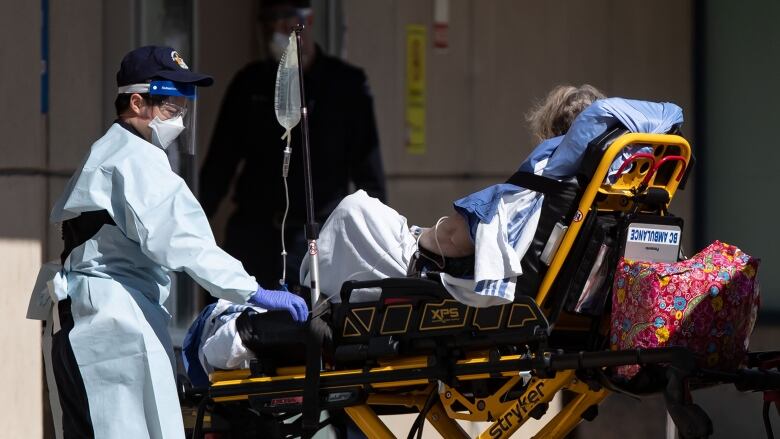 A B.C. Ambulance Service employee in protective equipment including an N95 mask, a face shield, goggles and gloves, moves a patient from an ambulance to the emergency department in April 2020.