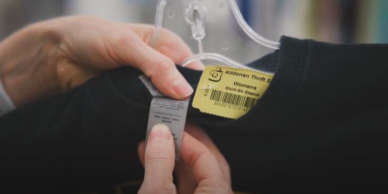 Woman's hand holds sweatshirt in store on hanger. The tag and price tag are visible