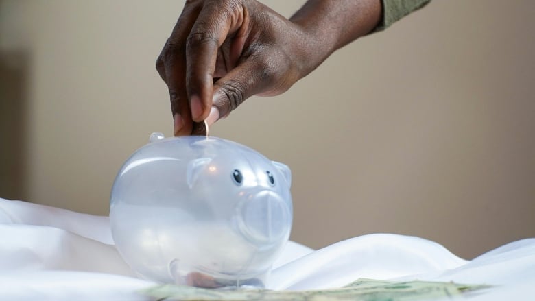 A hand putting a coin in a piggy bank. 