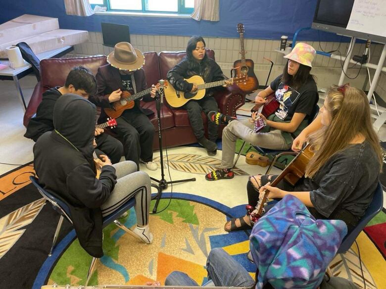 A group of youth sit in a circle. They are playing instruments. 