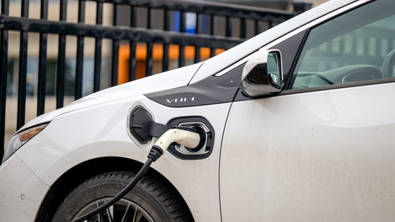 A charger is plugged into the side of a white electric vehicle.